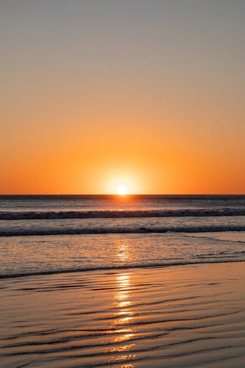 the sun is setting over the ocean on the beach